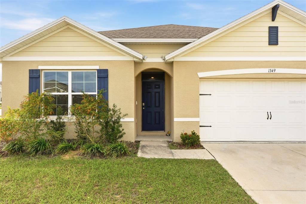 A single-story house with a beige stucco exterior, blue shutters, a dark door, and a garage — 1349 SUGARWOOD STREET, DAVENPORT, FL