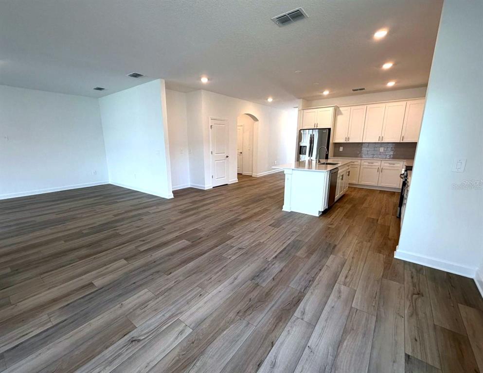 An open-concept living area features wood-look flooring and a kitchen with white cabinetry — 7867 POPLIN ST STREET, KISSIMMEE, FL