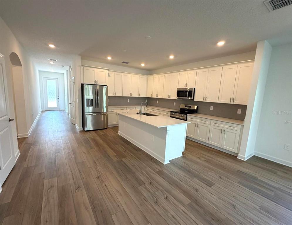 A modern kitchen features white cabinetry, stainless steel appliances, a center island, and wood flooring — 7867 POPLIN ST STREET, KISSIMMEE, FL