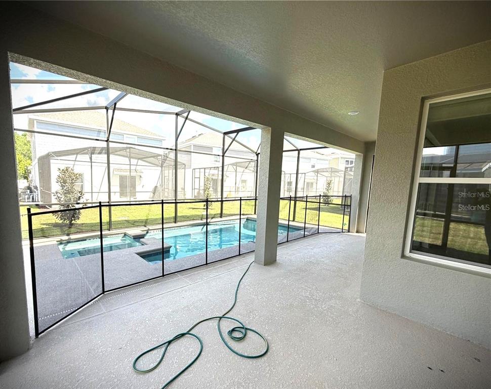 A covered patio overlooks a swimming pool enclosed by a screen cage and safety fence — 7867 POPLIN ST STREET, KISSIMMEE, FL