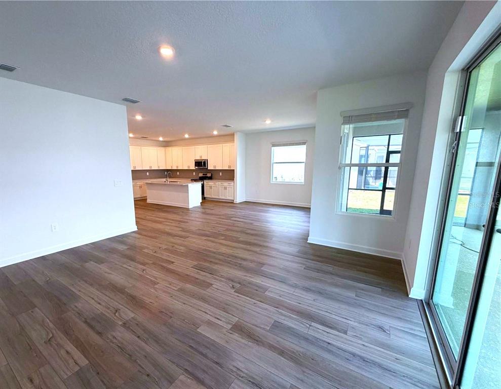 An open-concept living area with wood-look flooring leads to a kitchen with white cabinetry — 7867 POPLIN ST STREET, KISSIMMEE, FL