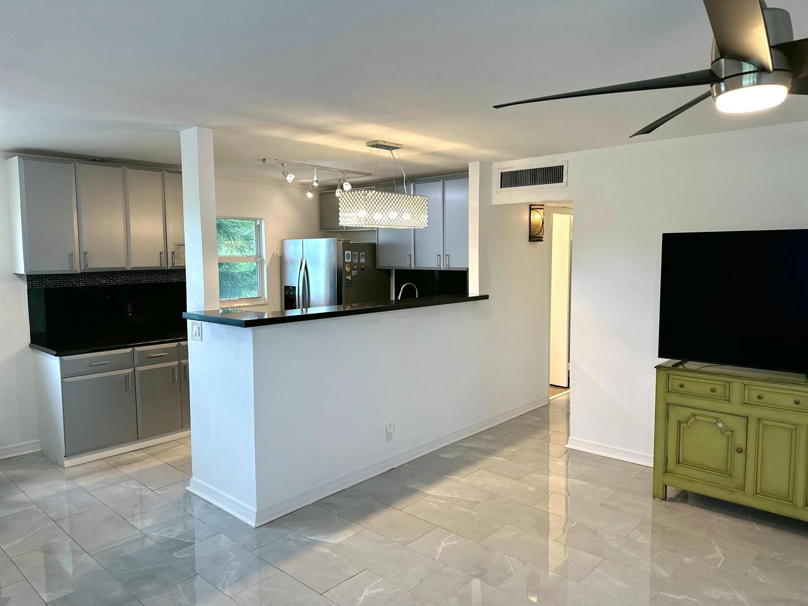 A kitchen with gray cabinets and black countertops opens to a living area with tile floors — 196 Tuscany C Lane, Delray Beach FL 33446, DELRAY BEACH, FL