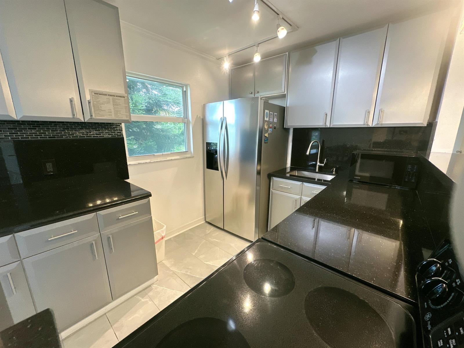 A kitchen features gray cabinets, black countertops, stainless steel appliances, and a window — 196 Tuscany C Lane, Delray Beach FL 33446, DELRAY BEACH, FL