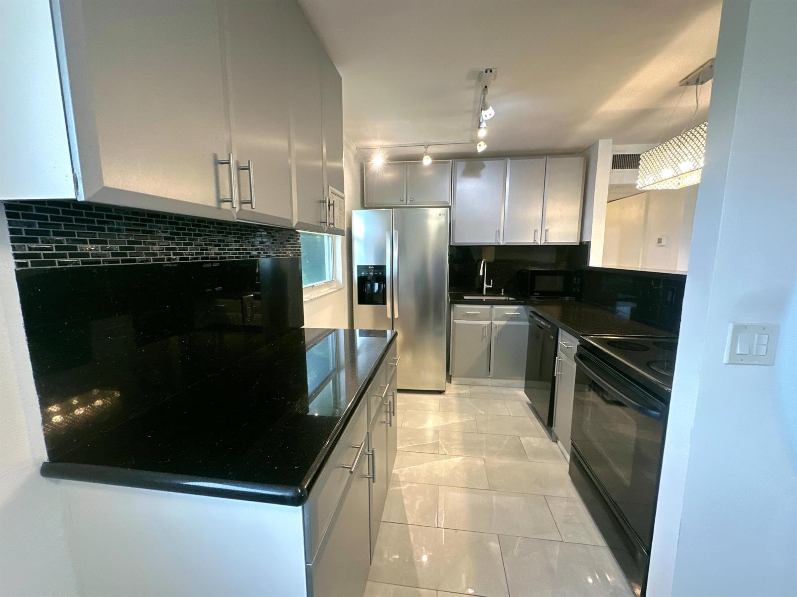 A modern kitchen features grey cabinets, black countertops, stainless steel appliances, and light tile flooring — 196 Tuscany C Lane, Delray Beach FL 33446, DELRAY BEACH, FL