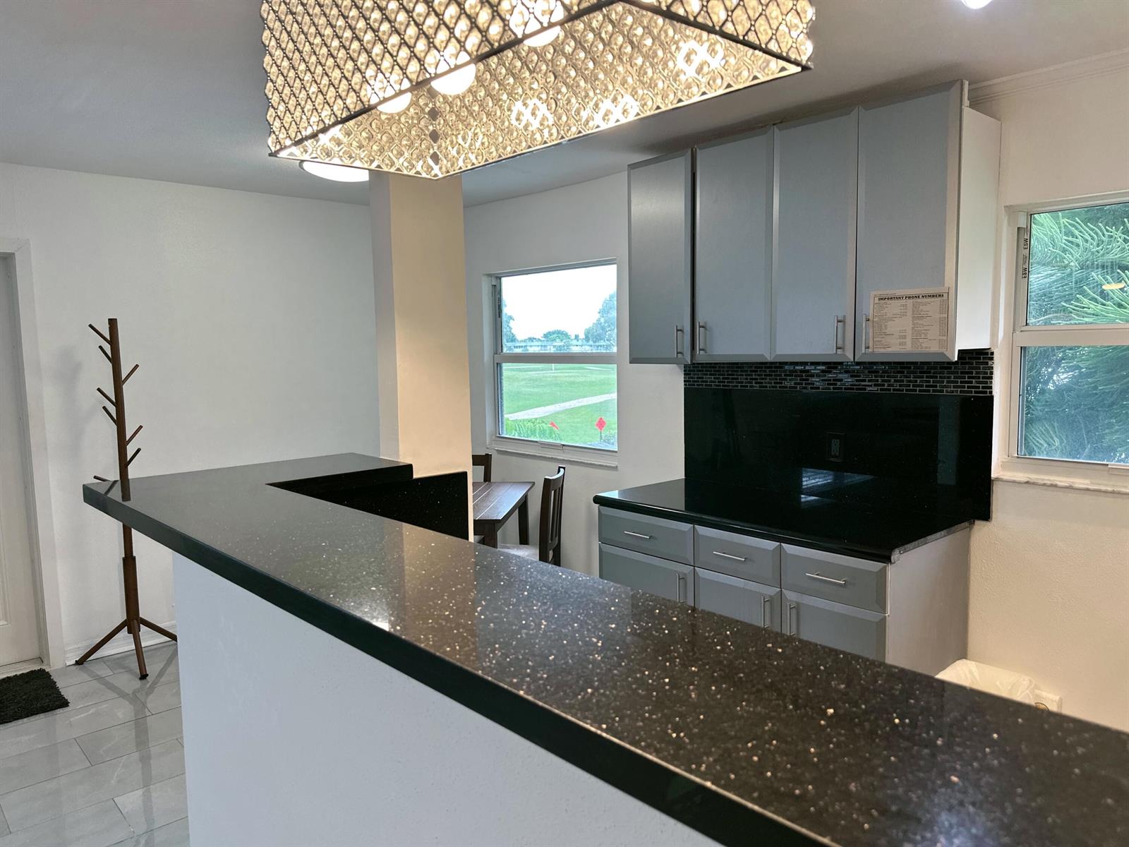 A kitchen features gray cabinets, black countertops, a tile backsplash, and a crystal chandelier — 196 Tuscany C Lane, Delray Beach FL 33446, DELRAY BEACH, FL