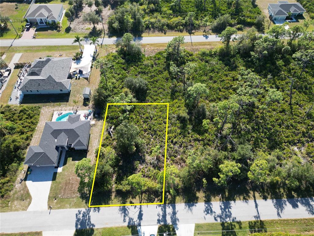 An aerial view shows a vacant, wooded residential lot outlined in yellow next to houses — 13417 YAGER LANE, PORT CHARLOTTE, FL