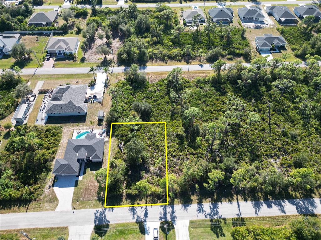 An aerial view shows a vacant, wooded residential lot outlined in yellow next to a house — 13417 YAGER LANE, PORT CHARLOTTE, FL