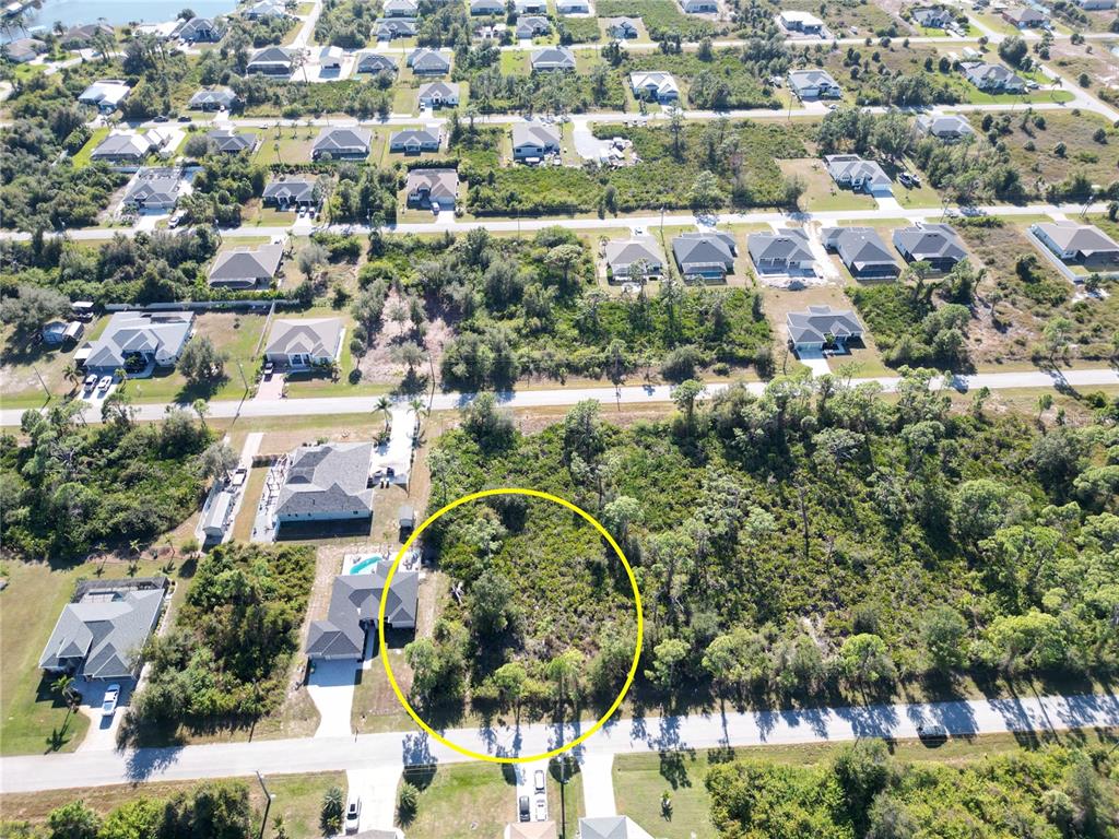 An aerial view shows a vacant, wooded residential lot circled in yellow next to houses — 13417 YAGER LANE, PORT CHARLOTTE, FL
