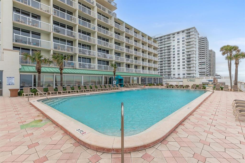 A rectangular swimming pool sits on a paved patio in front of a multi-story hotel — 2700 N ATLANTIC AVENUE UNIT 819, DAYTONA BEACH, FL