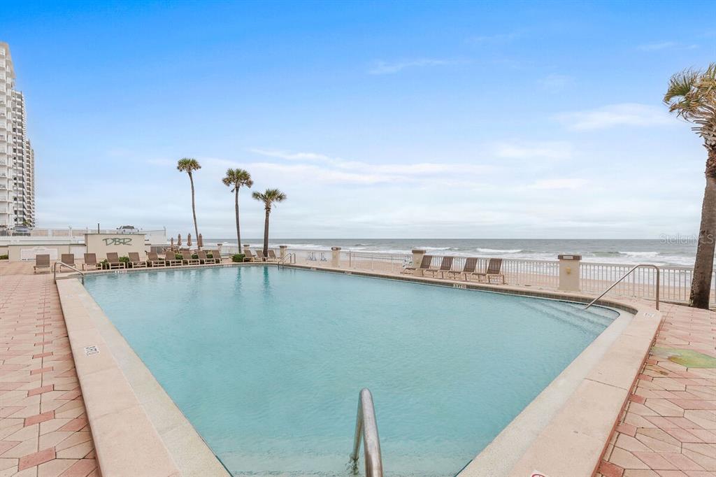 An outdoor swimming pool overlooks the ocean with lounge chairs on a sandy beach — 2700 N ATLANTIC AVENUE UNIT 819, DAYTONA BEACH, FL