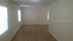 An empty room features light-colored walls, wood-look flooring, two windows, and a white door — 2319 CARLTON DRIVE, ORLANDO, FL