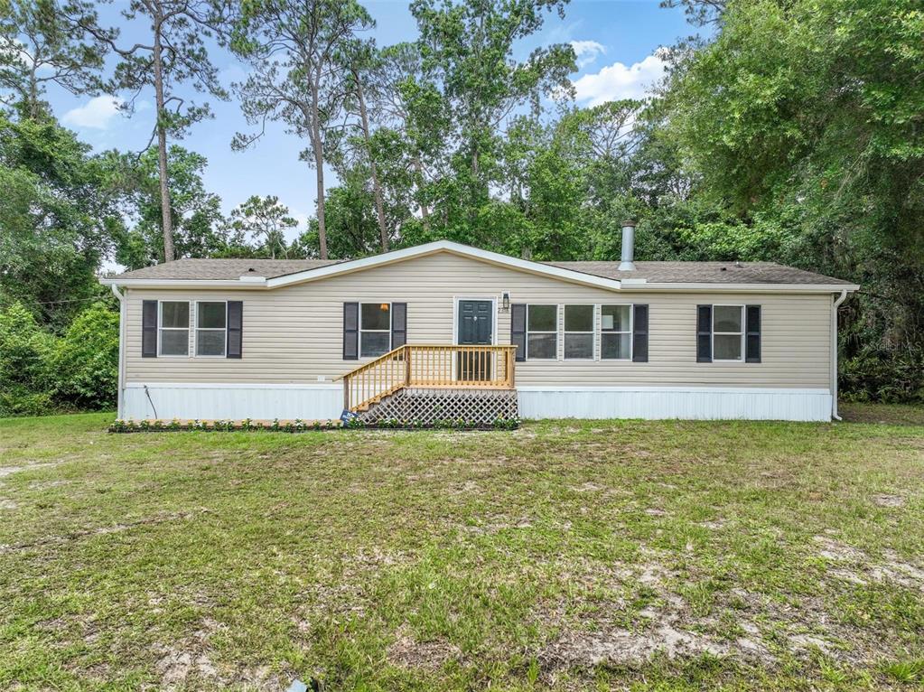 A single-story manufactured home with beige siding and a wooden front porch sits on grass — 2318 COCONUT BOULEVARD, BUNNELL, FL