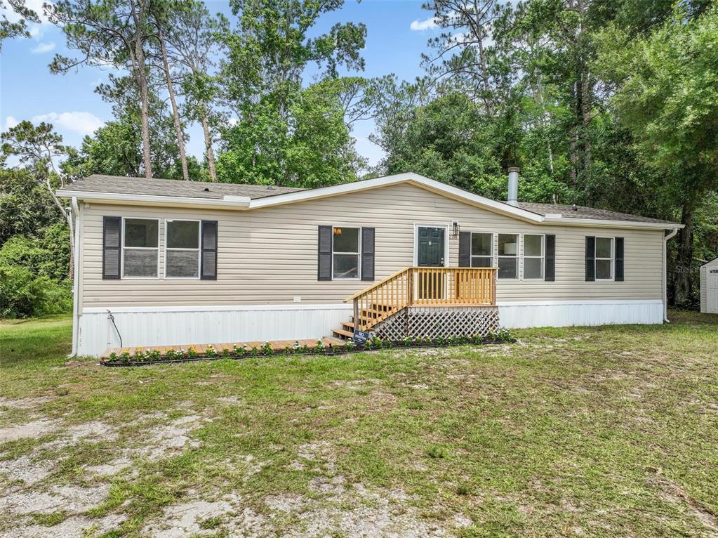 A single-story manufactured home with beige siding, black shutters, and a wooden front porch — 2318 COCONUT BOULEVARD, BUNNELL, FL