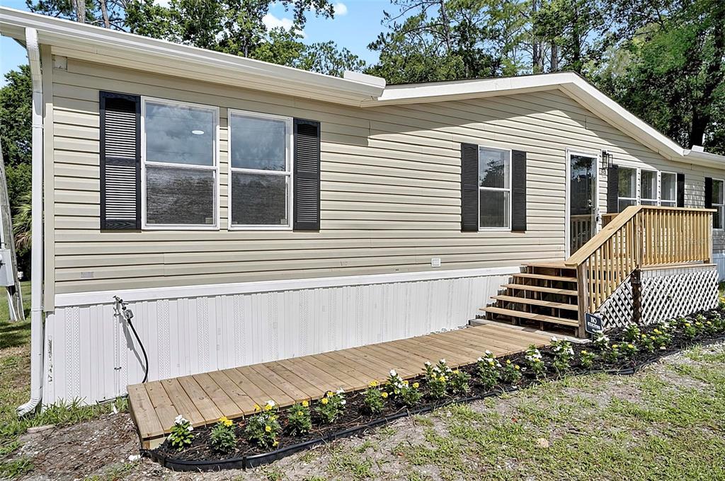 The exterior of a tan manufactured home features a wooden deck, stairs, and flower beds — 2318 COCONUT BOULEVARD, BUNNELL, FL