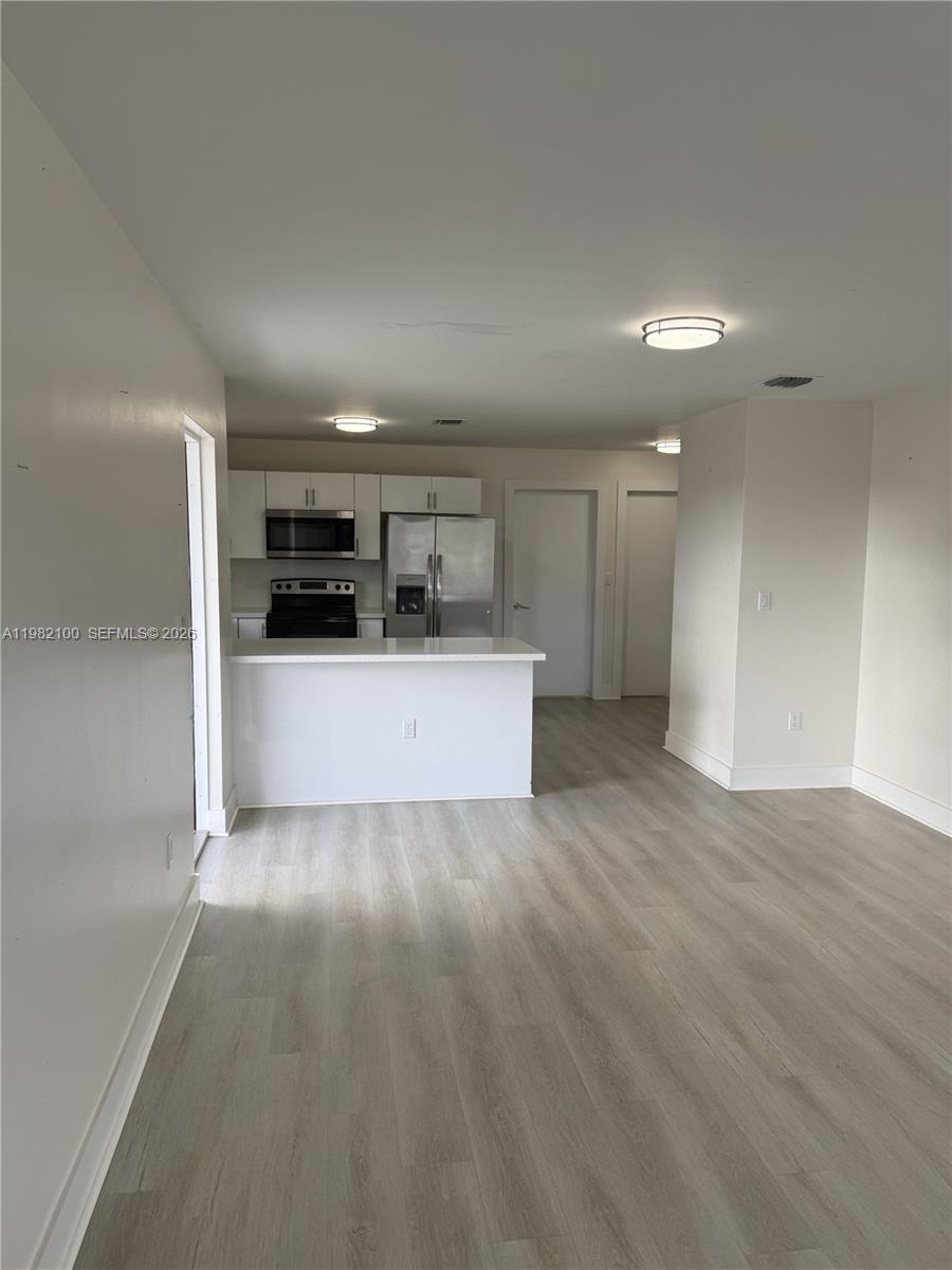An open-concept kitchen features white cabinetry, stainless steel appliances, and light wood-look flooring — 10384 SW 173rd St # 2, Miami FL 33157, MIAMI, FL