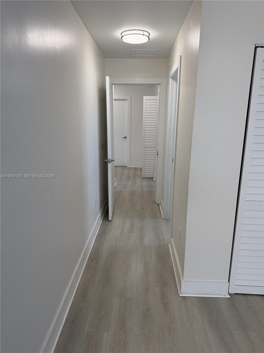 A hallway with light wood-look flooring leads to an open doorway and a closet — 10384 SW 173rd St # 2, Miami FL 33157, MIAMI, FL