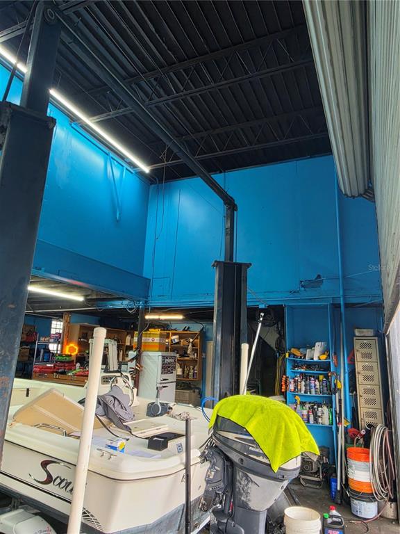A boat sits inside a garage with blue walls, an exposed ceiling, and a vehicle lift — 1942 E HILLSBOROUGH AVENUE, TAMPA, FL