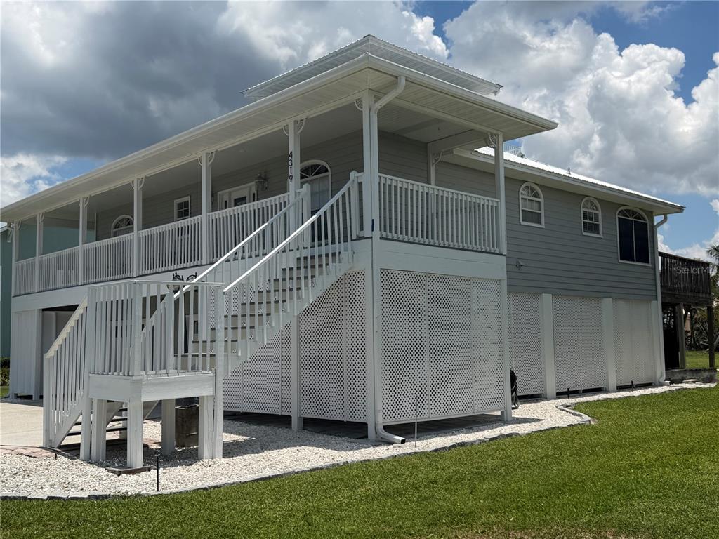A two-story elevated house with light gray siding, a white wraparound porch, and lattice skirting — 4319 15TH WAY, PALMETTO, FL