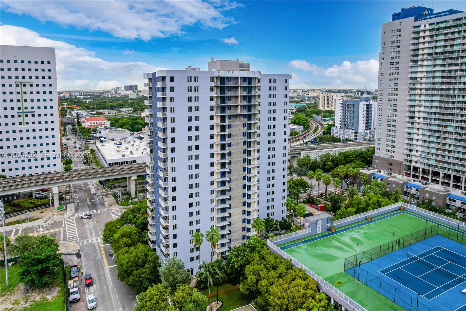 An aerial view shows a tall residential building next to a tennis court and elevated train tracks — 850 N Miami Ave # 408, Miami FL 33136, MIAMI, FL