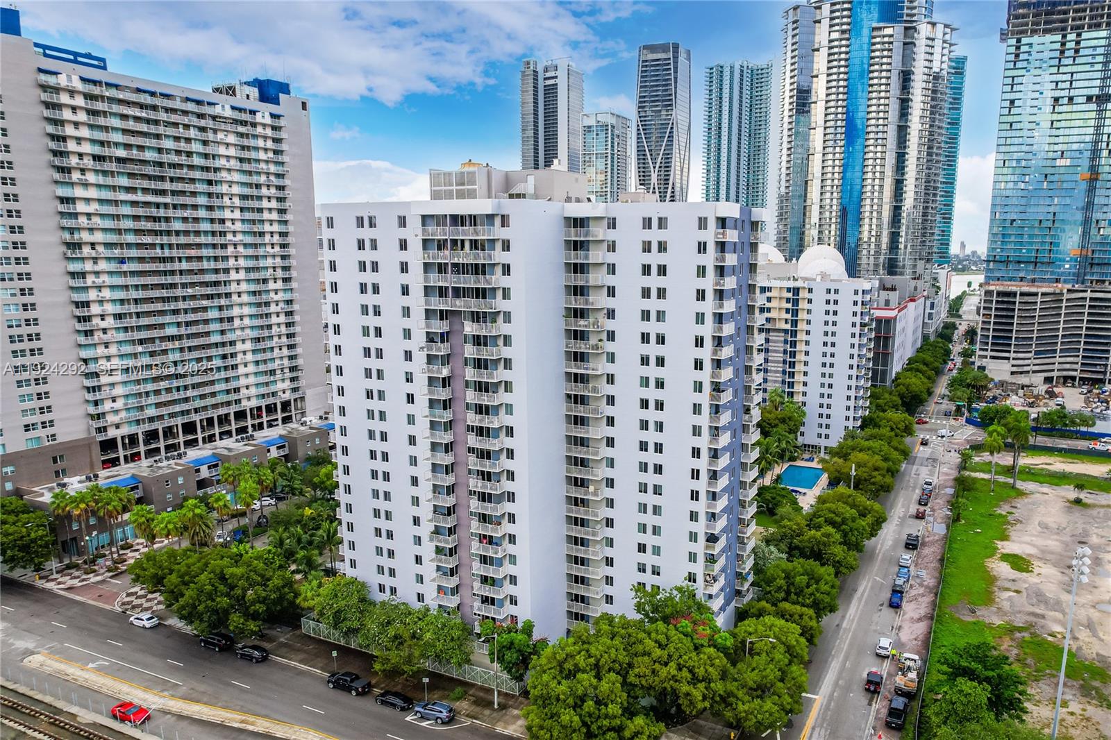 An aerial view of a white high-rise apartment building surrounded by trees and city skyscrapers — 850 N Miami Ave # 408, Miami FL 33136, MIAMI, FL