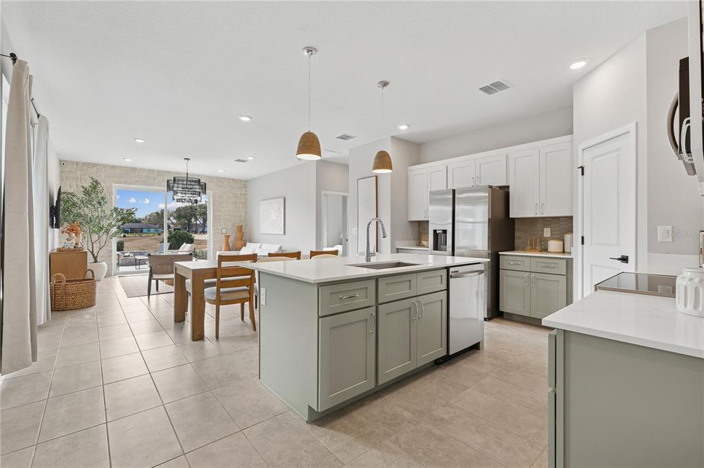 A kitchen with sage green cabinets and a white island opens to a dining area — 4474 NW 37TH STREET ROAD, OCALA, FL