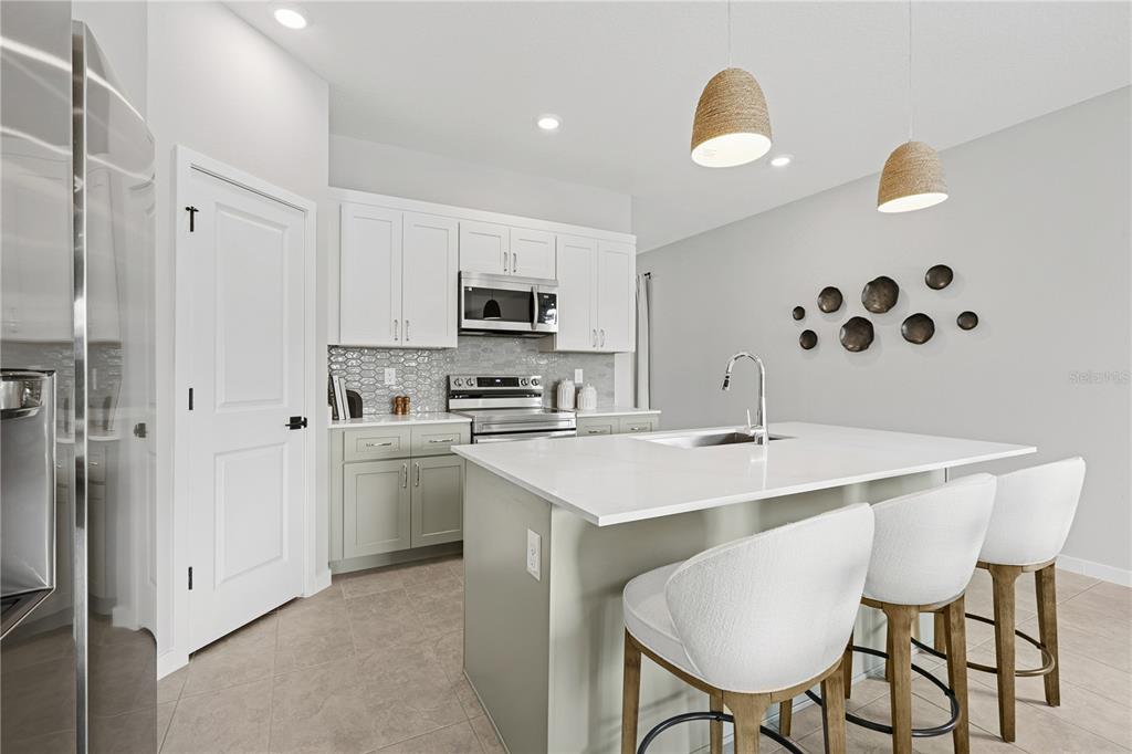 A modern kitchen features white upper cabinets, sage green lower cabinets, and a central island — 4474 NW 37TH STREET ROAD, OCALA, FL