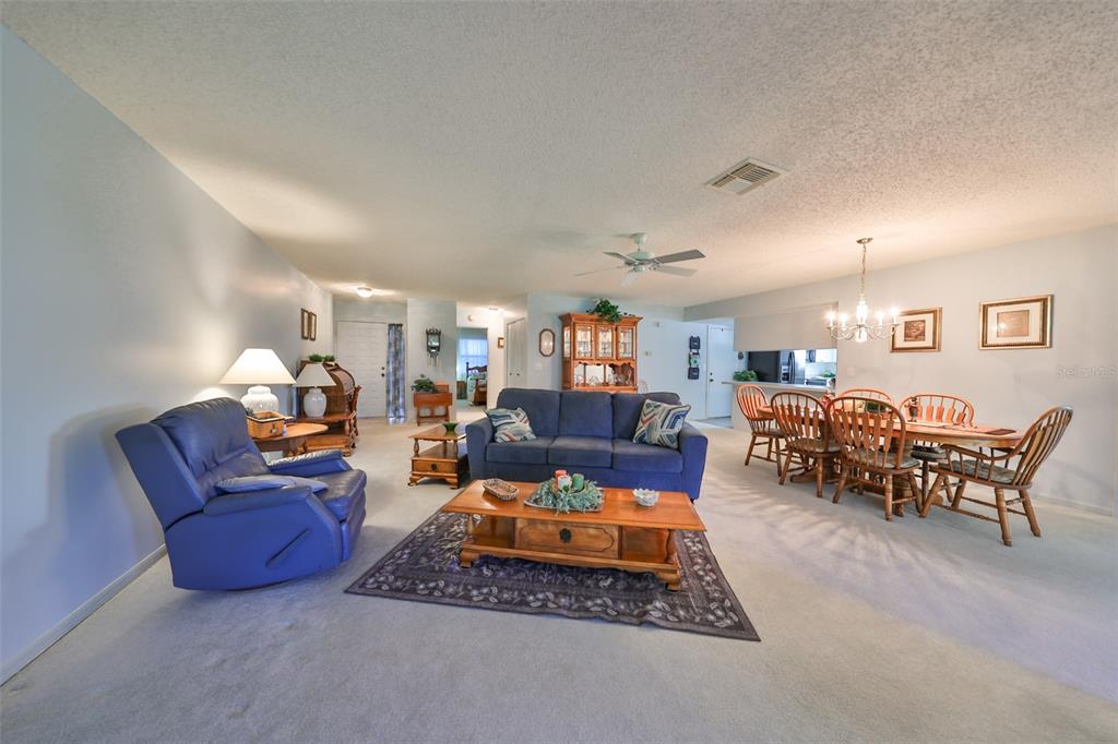A living and dining room area features blue furniture, a wooden coffee table, and carpet — 2414 LOCKSLEY STREET, SUN CITY CENTER, FL
