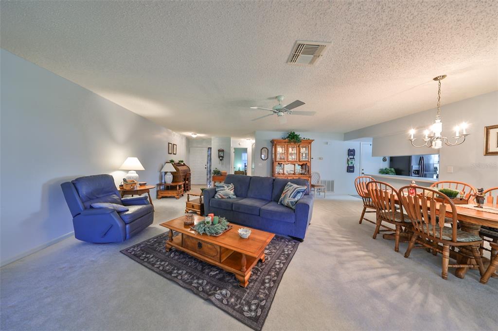 A living room with a blue sofa and recliner, a wooden coffee table, and dining area — 2414 LOCKSLEY STREET, SUN CITY CENTER, FL