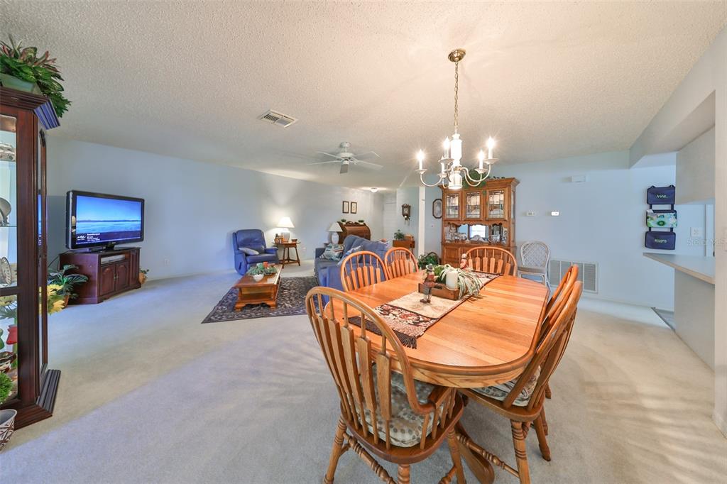 A dining area with a wooden table and chairs opens into a carpeted living room — 2414 LOCKSLEY STREET, SUN CITY CENTER, FL