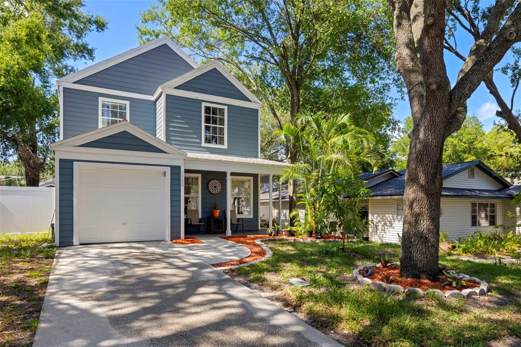 A two-story blue house with a white garage and a front porch sits near trees — 7508 WAKULLA DRIVE, TEMPLE TERRACE, FL