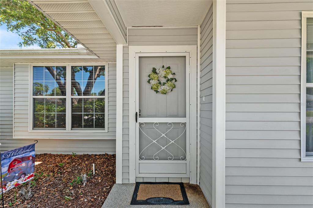 The exterior view shows a grey-sided house entrance with a screen door and welcome mat — 8038 SW 108TH LOOP, OCALA, FL