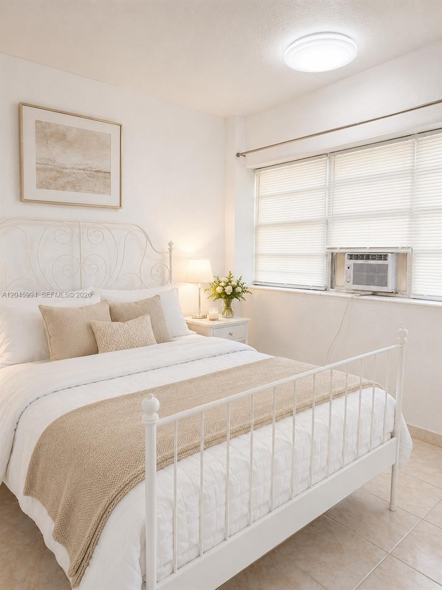 A bedroom features a white metal bed frame, neutral bedding, and a window air conditioner — HALLANDALE BEACH, FL