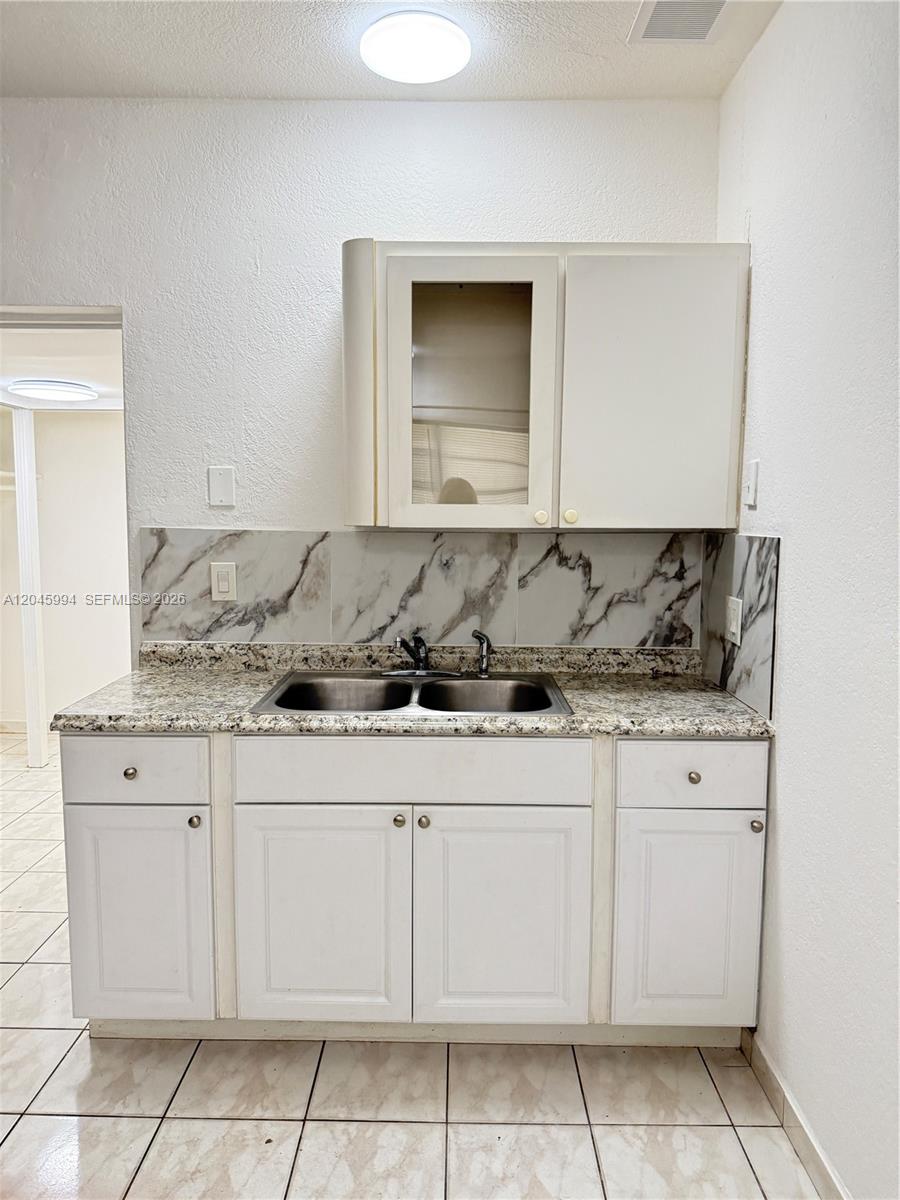 A kitchen features white cabinets, a granite countertop, and a marble-patterned backsplash — HALLANDALE BEACH, FL