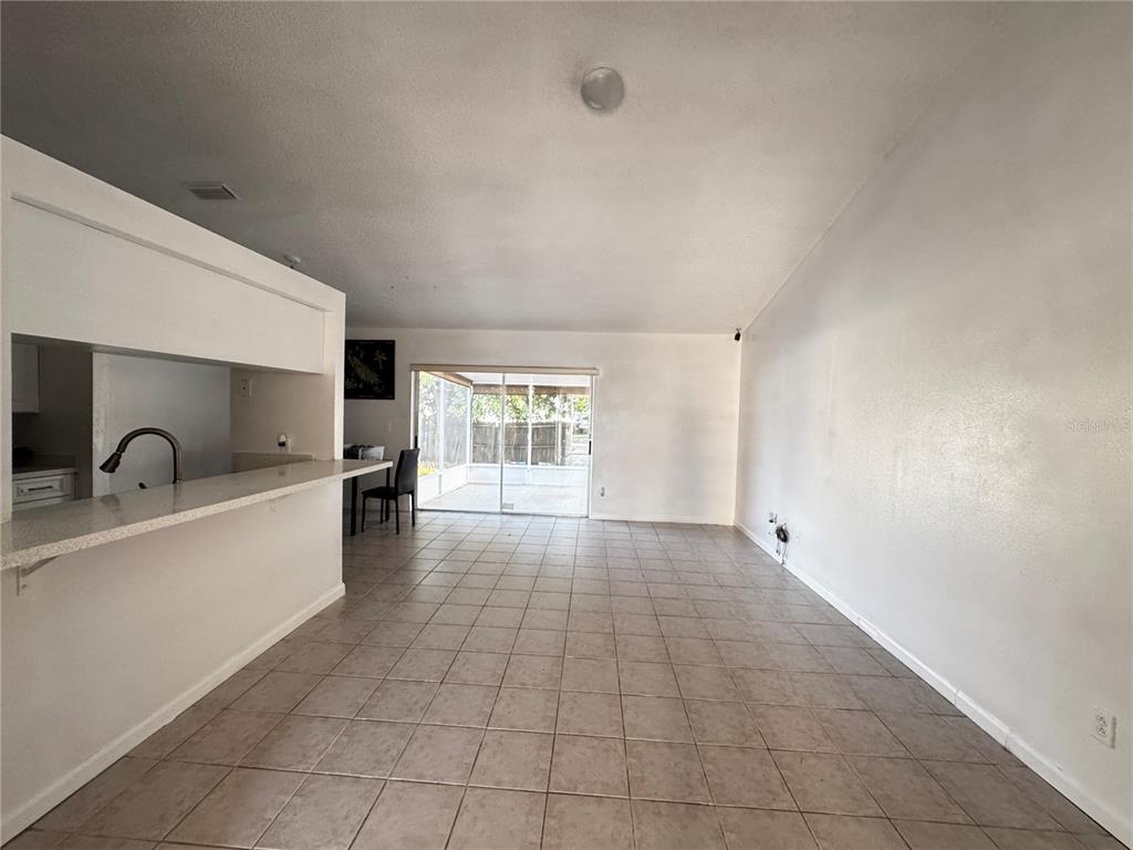 An open-concept living and dining area features tiled floors, a kitchen pass-through, and sliding glass doors — 9213 CAMINO VILLA BOULEVARD, TAMPA, FL
