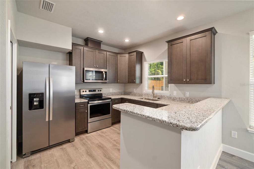 A kitchen with dark wood cabinets, granite countertops, stainless steel appliances, and light wood flooring — 622 NW 3RD AVENUE UNIT 7, GAINESVILLE, FL