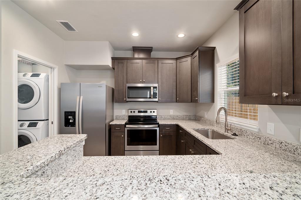 A kitchen with dark wood cabinets, granite countertops, stainless steel appliances, and a stacked washer-dryer — 622 NW 3RD AVENUE UNIT 7, GAINESVILLE, FL