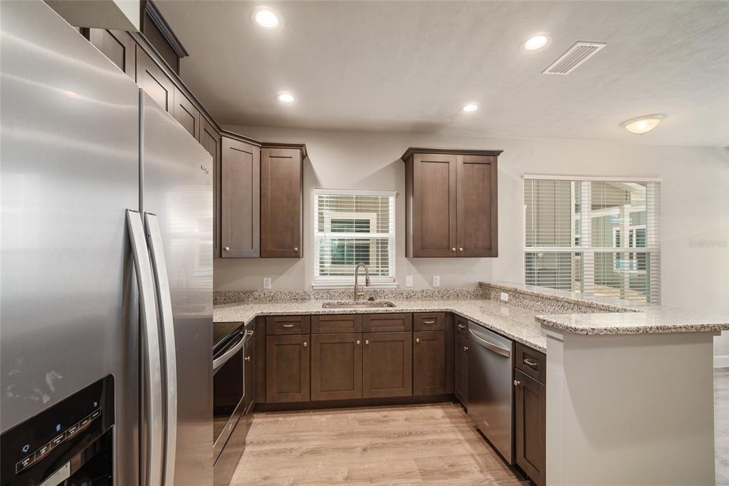 A kitchen features dark wood cabinets, granite countertops, stainless steel appliances, and wood-look flooring — 622 NW 3RD AVENUE UNIT 7, GAINESVILLE, FL