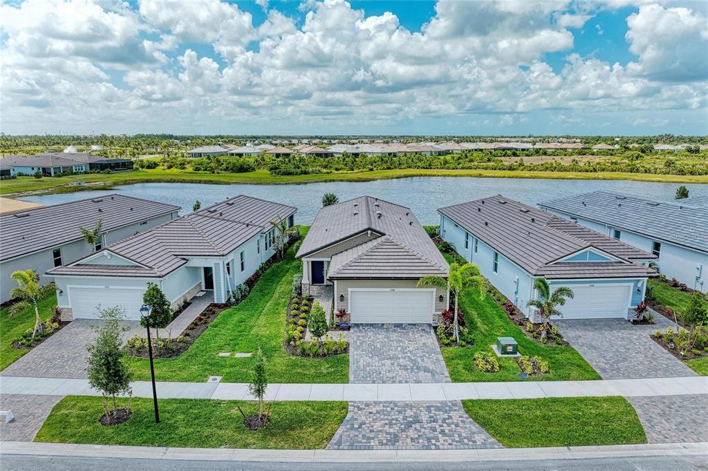 An aerial view shows three suburban houses with tiled roofs situated along a waterfront — 11566 BOUNDLESS TERRACE, VENICE, FL