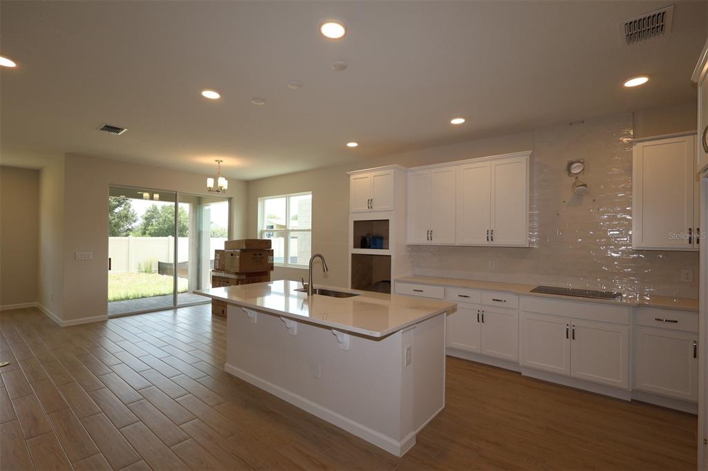 A modern kitchen features white cabinets, a central island, stainless steel appliances, and wood-look flooring — 6753 YELLOW WARBLER BEND, ST CLOUD, FL