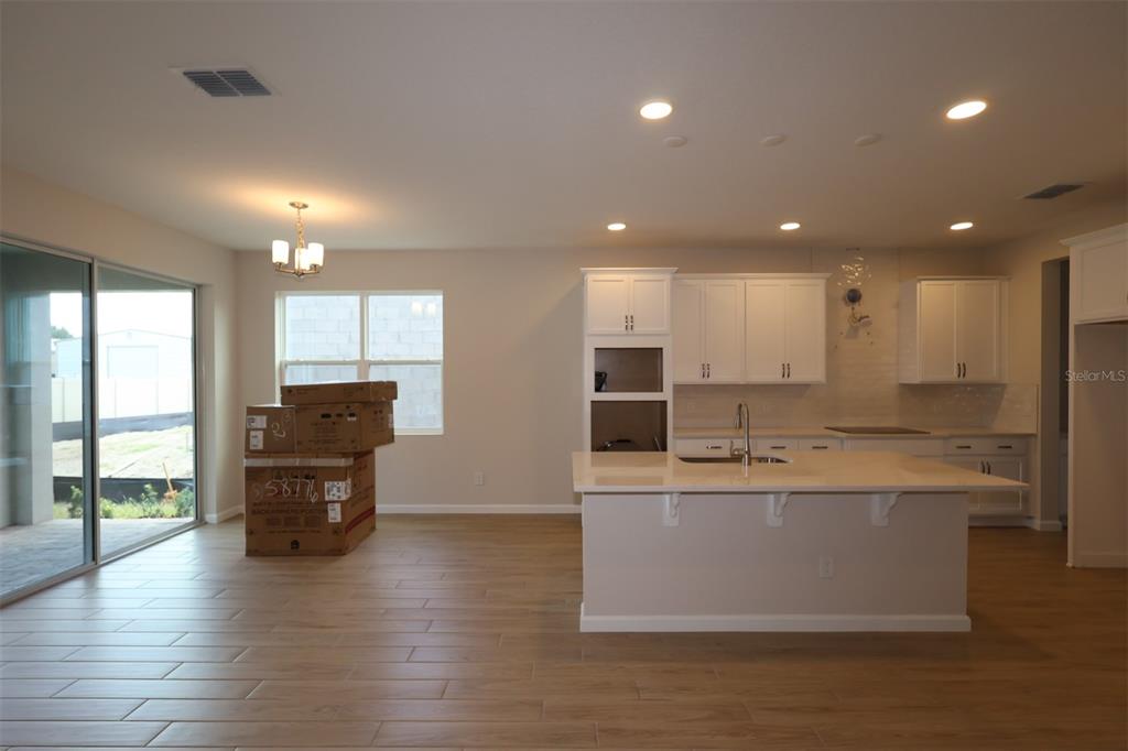 A modern kitchen features white cabinetry, a central island with a sink, and tile flooring — 6753 YELLOW WARBLER BEND, ST CLOUD, FL