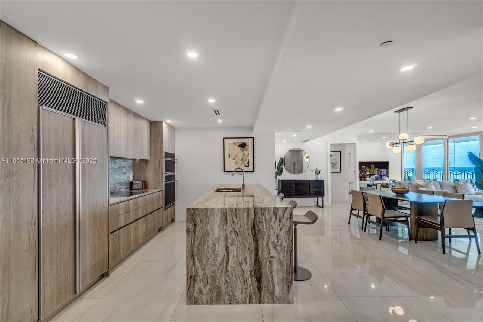 A modern kitchen features a large stone island, wood-toned cabinetry, and an adjacent dining area — 1500 Ocean Drive # 1003, Miami Beach FL 33139, MIAMI BEACH, FL