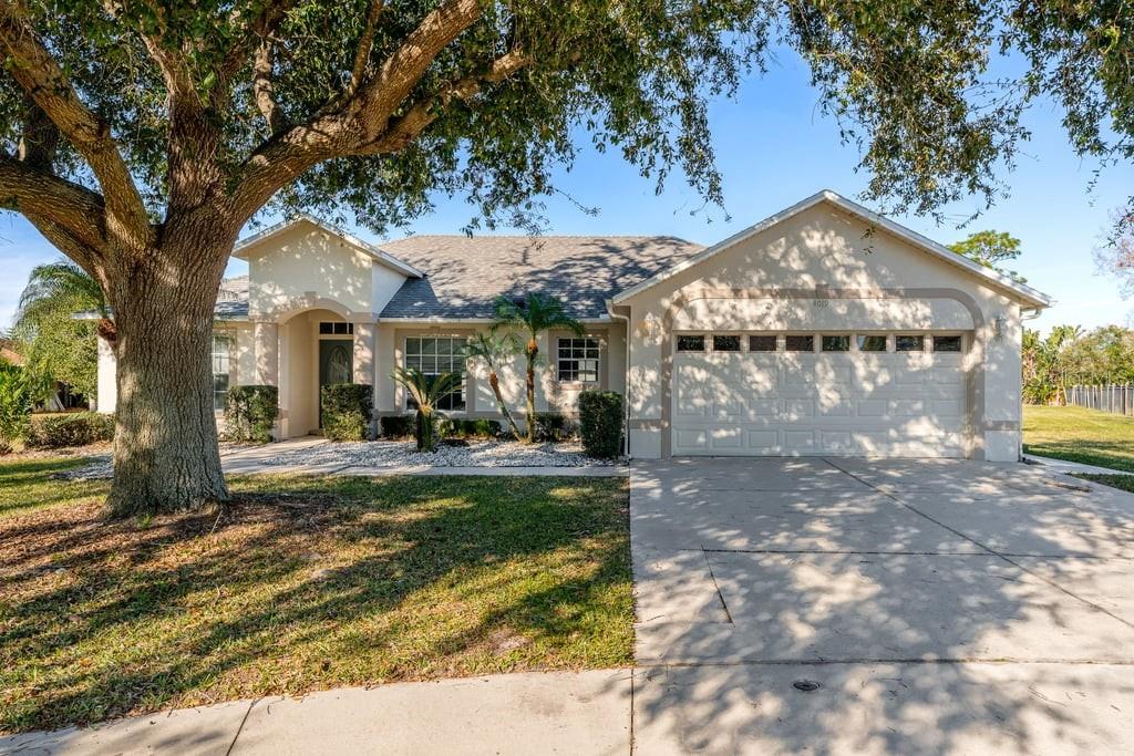 A single-story house with a two-car garage, a large oak tree, and a concrete driveway — 4019 GEORGETOWN COURT, ST CLOUD, FL