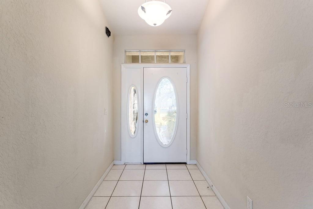 An entryway features a white front door with a sidelight, tile flooring, and a light fixture — 4019 GEORGETOWN COURT, ST CLOUD, FL