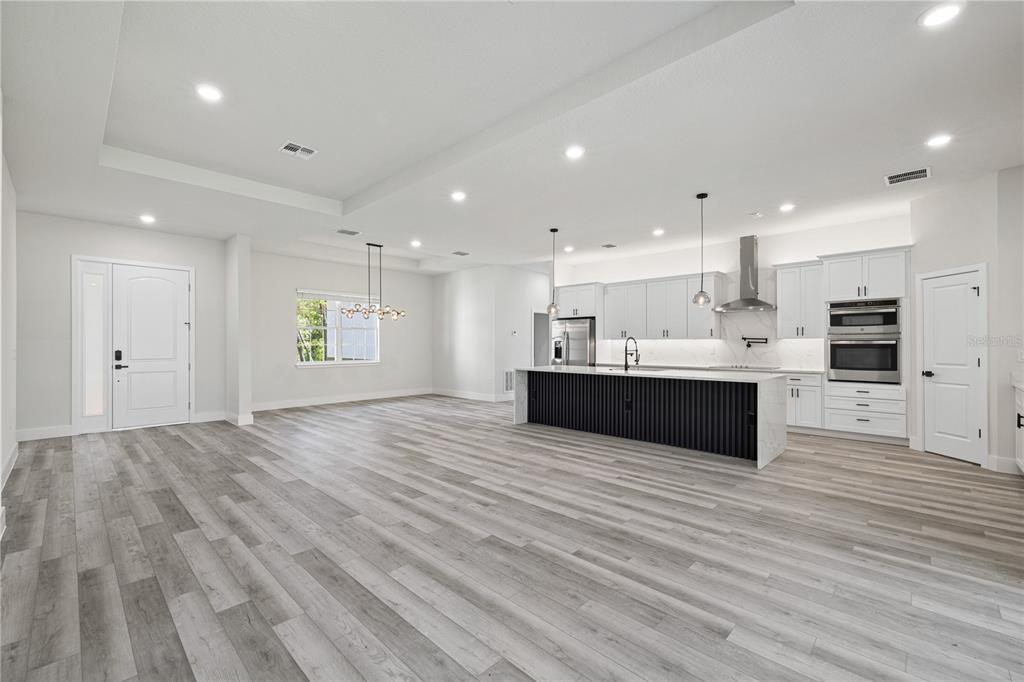 A modern open-concept kitchen and living area featuring light wood floors and a dark-paneled island — 8268 SW 122ND AVENUE, DUNNELLON, FL