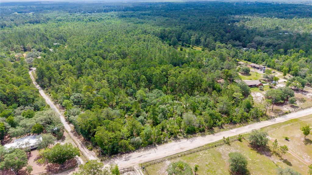 An aerial view shows a wooded lot bordered by dirt roads and nearby residential buildings — GOLDEN OAK LANE, KEYSTONE HEIGHTS, FL