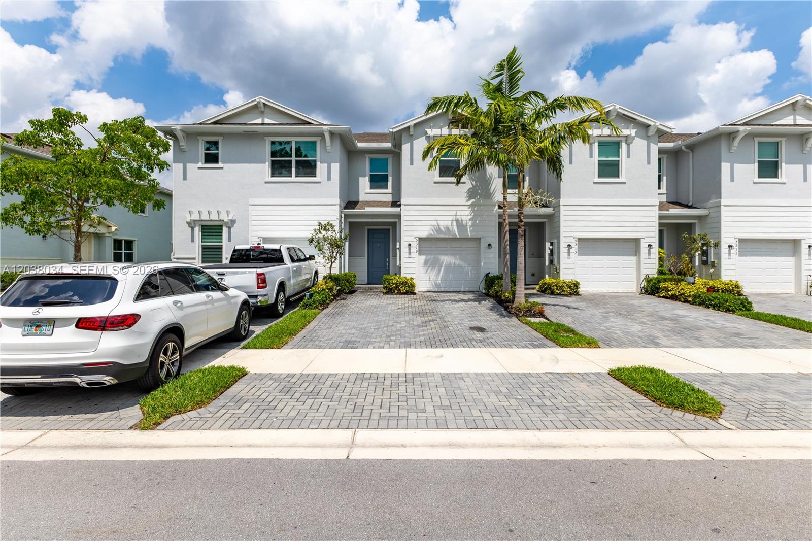 A row of light-colored townhouses features paved driveways, attached garages, and a palm tree — 5319 Flannigan Way # 0, Lake Worth FL 33463, LAKE WORTH, FL