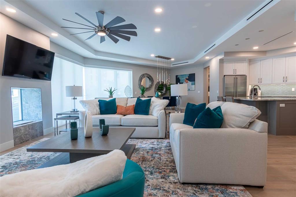 A living room with a ceiling fan, white sofas, teal accents, and an open kitchen — 1140 SEASIDE DRIVE UNIT 101, SARASOTA, FL