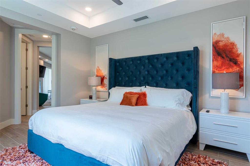 A bedroom features a tufted blue headboard, white nightstands, and abstract orange wall art — 1140 SEASIDE DRIVE UNIT 101, SARASOTA, FL
