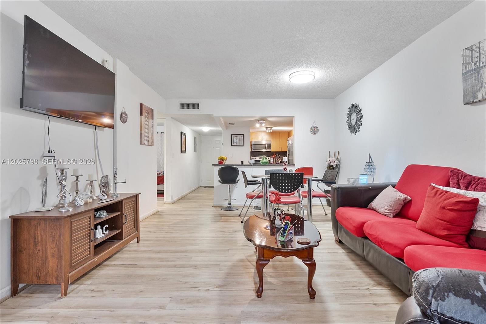 A living room features light wood flooring, a red sofa, and an open-concept kitchen — 10000 NW 80th Ct # 2245, Hialeah Gardens FL 33016, HIALEAH GARDENS, FL