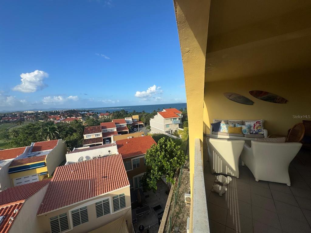 A balcony with outdoor furniture overlooks a residential neighborhood and the ocean in the distance — 295 PALMAS INNWAY UNIT 323, HUMACAO, PR